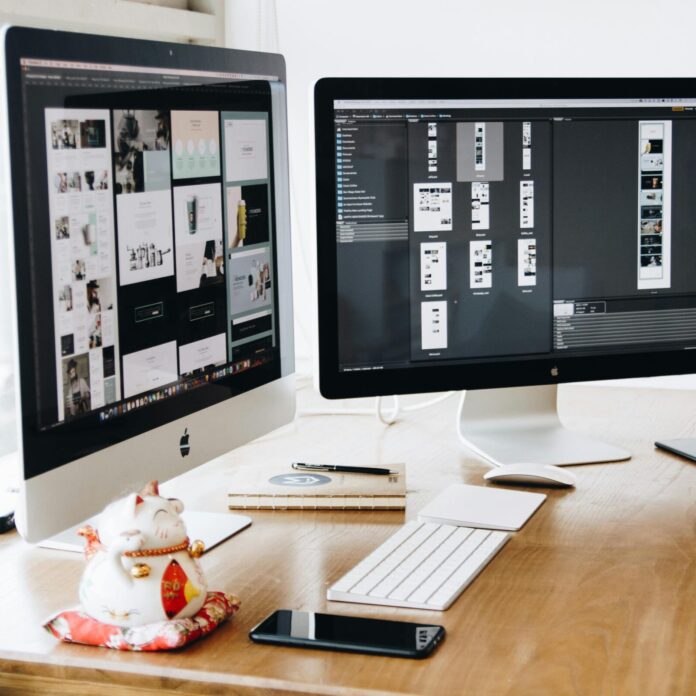 Two Imac's With Keyboard and Phones on Desk
